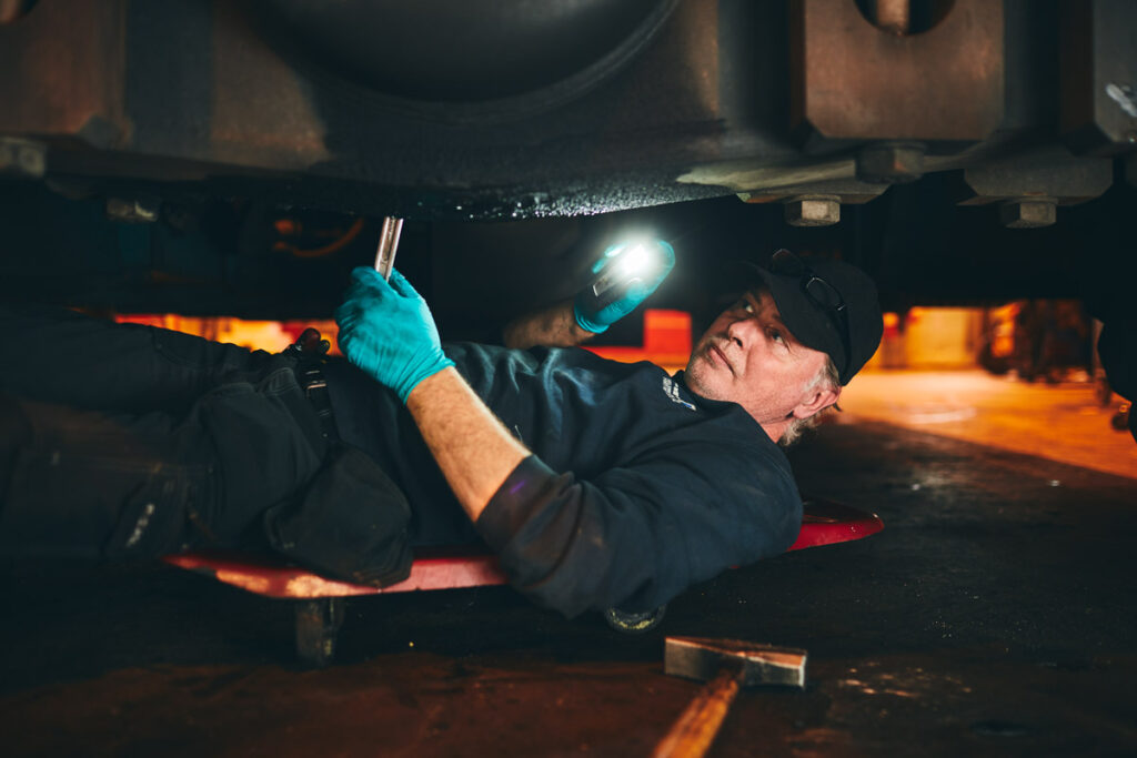 En medarbetare på verkstaden ligger under en bil och håller in en skiftnyckel