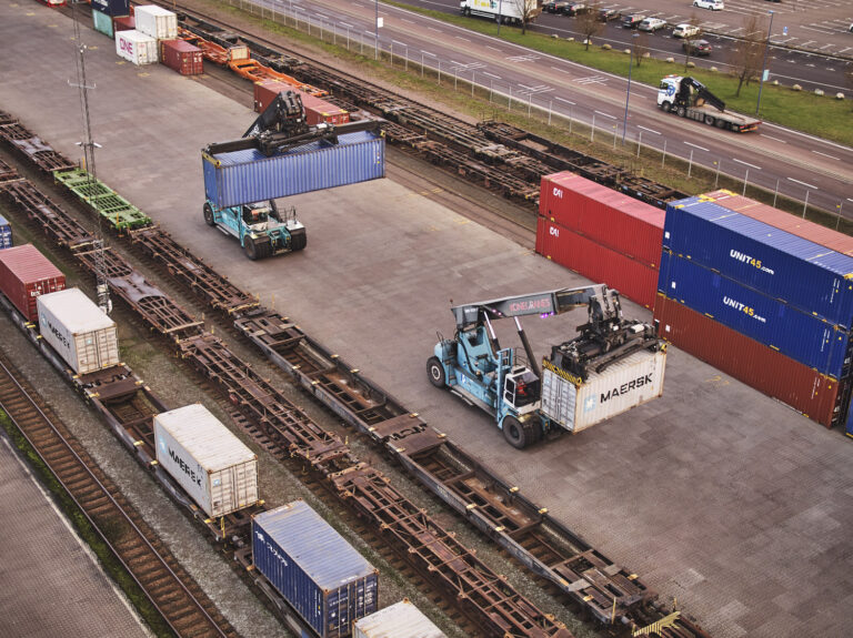 Two reachstackers driving with containers beside rail tracks