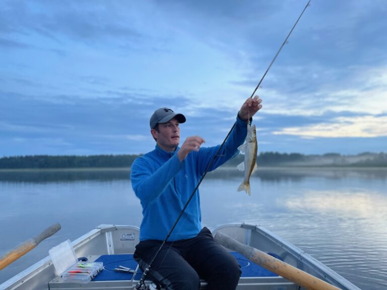 Man i keps sitter och fiskar i en båt med åror. På spöet sitter en fisk.