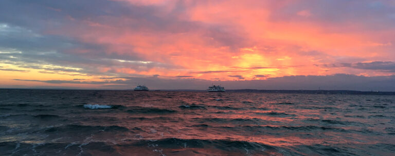Röd solnedgångshimmel över ett mörkt hav. Två båtar syns på havet