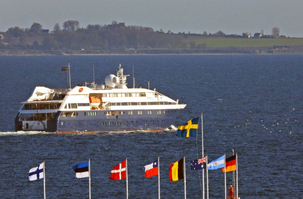 kryssare seglar i solnedgången. flaggor vajar i förgrunden och land syns i bakgrunden