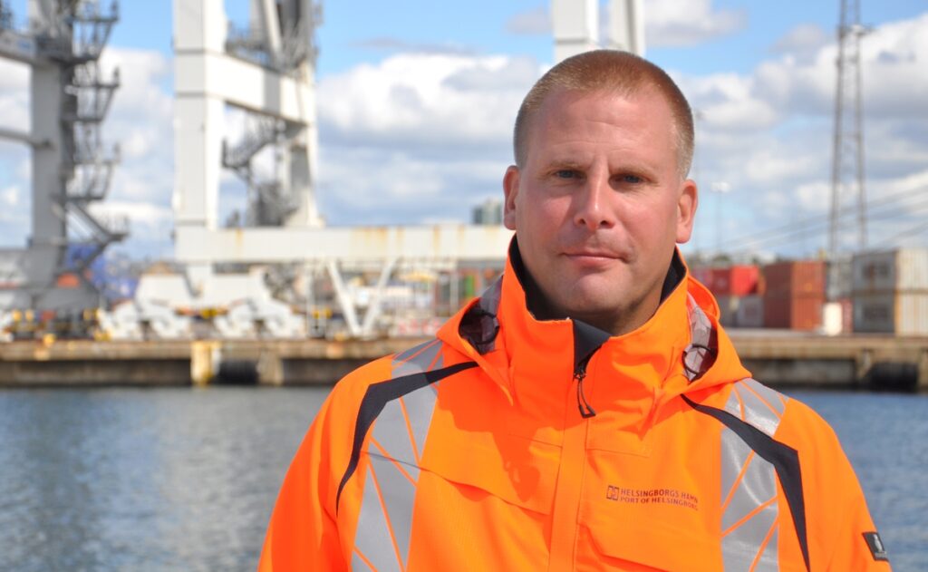 Man iklädd varseljacka stående vid kaj i containerterminal.